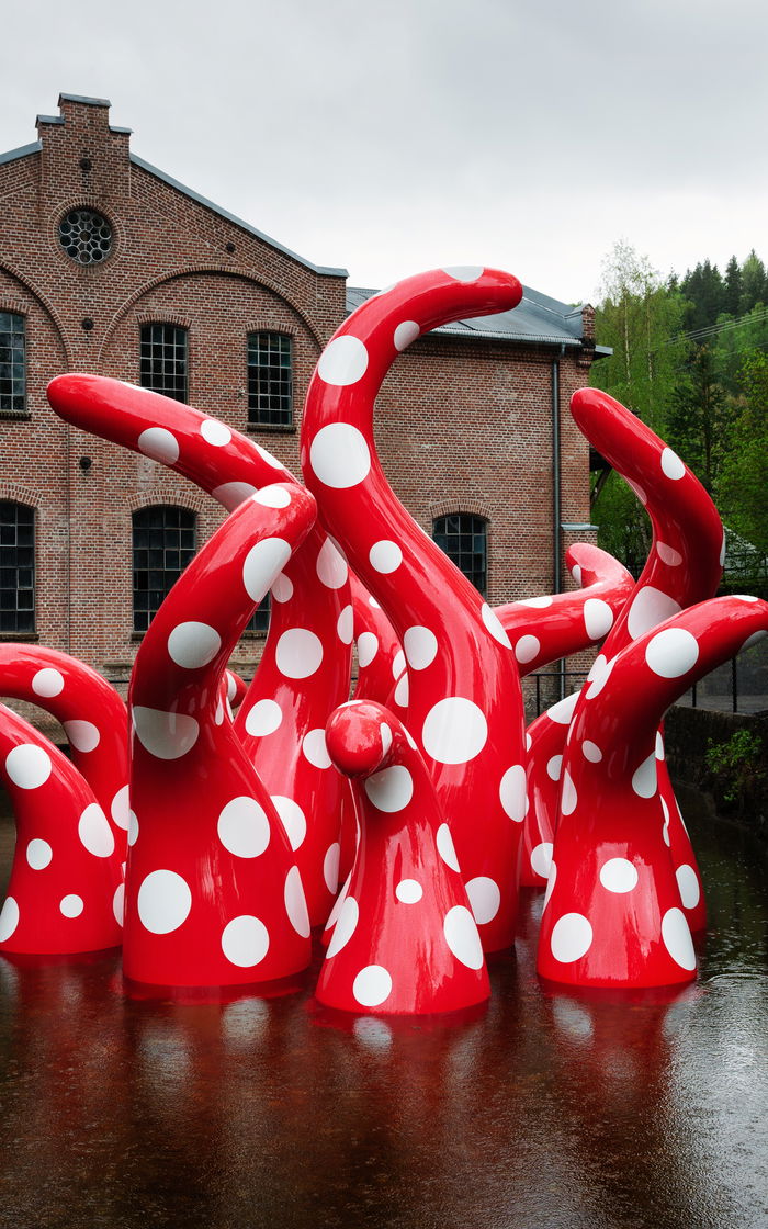 Sculpture by japaneese artist Yayoi Kusama showing octopuslike red and white dotty arms emerging up from the water.